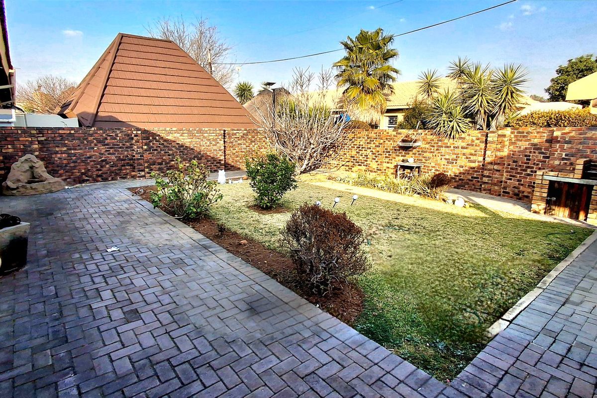 A private rear garden featuring a paved patio area, a built-in braai, and a lawn enclosed by a brick boundary wall.