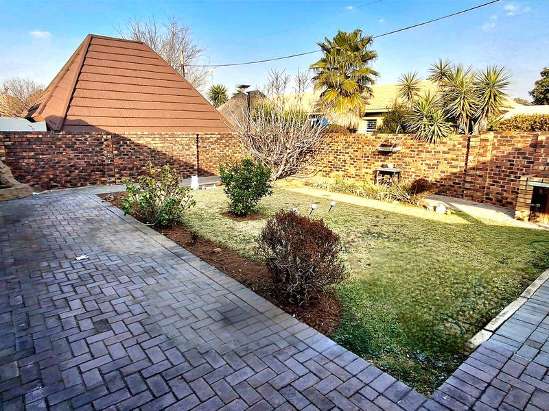 A private rear garden featuring a paved patio area, a built-in braai, and a lawn enclosed by a brick boundary wall.