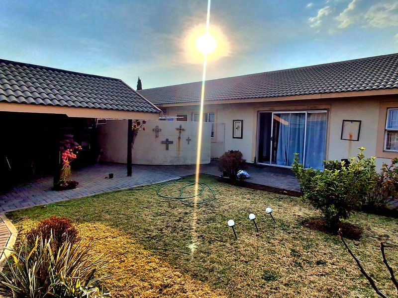 Rear exterior view of the townhouse featuring a paved patio area, built-in brick braai, small garden, and sliding door access to the main living space.