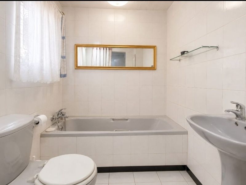 A functional bathroom featuring a bathtub, pedestal basin, and toilet with white wall tiles and neutral floor tiling.