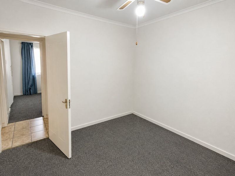 A clean, empty bedroom featuring neutral walls, grey carpeting, and a ceiling fan, offering a blank canvas for personalization.
