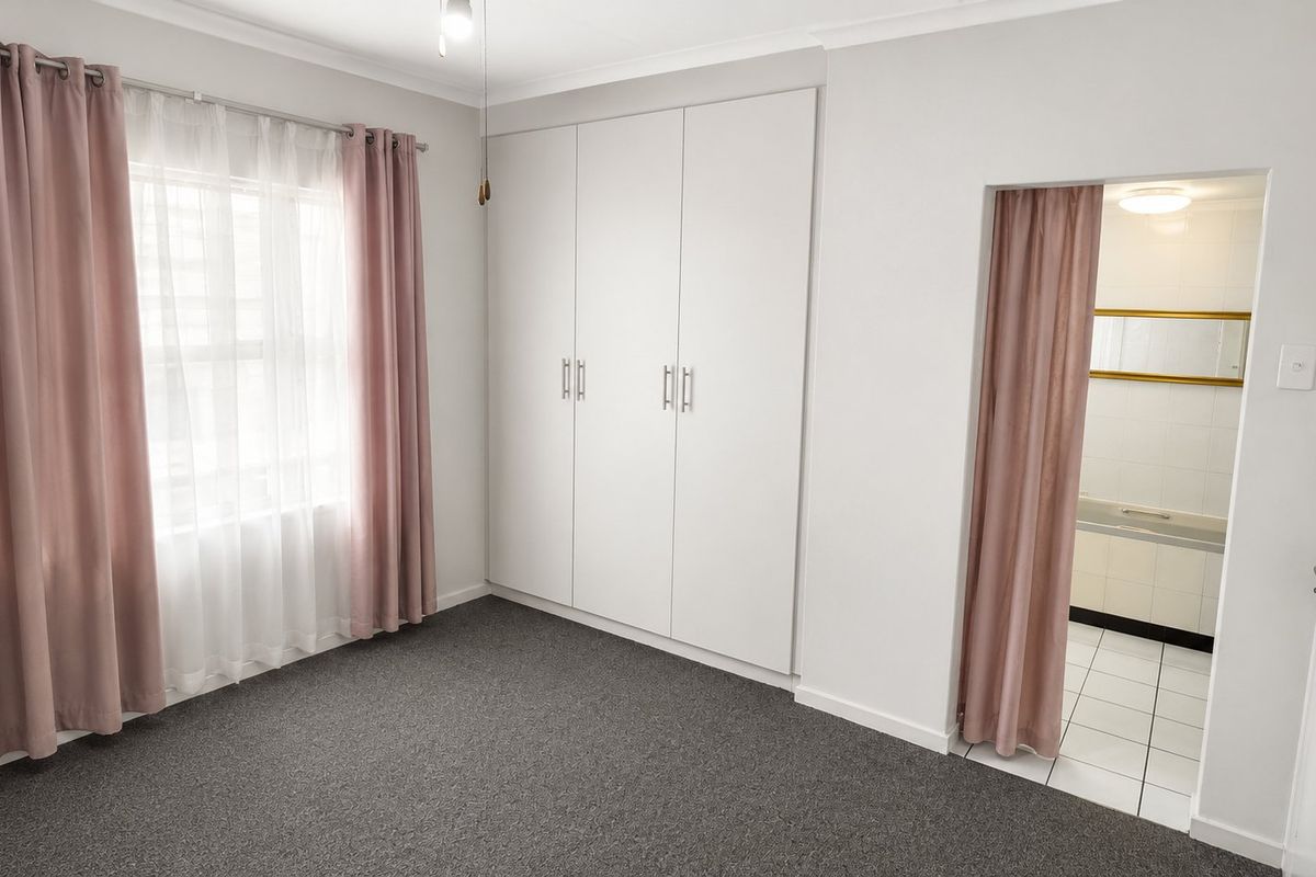 A clean, neutral bedroom featuring built-in cupboards, carpeted flooring, and direct access to an en-suite bathroom.