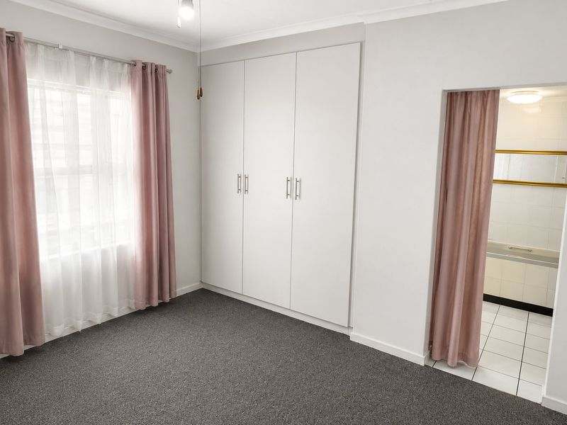 A clean, neutral bedroom featuring built-in cupboards, carpeted flooring, and direct access to an en-suite bathroom.