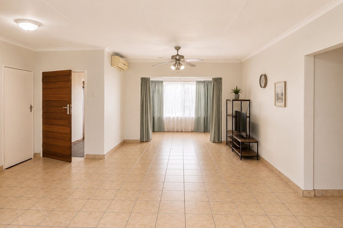 A spacious, neutrally painted living area featuring tiled flooring, a ceiling fan, and a wall-mounted air conditioning unit, offering a clean and versatile layout.