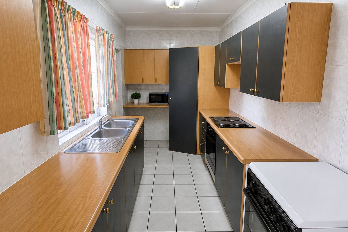 A functional galley-style kitchen featuring laminate countertops, built-in cabinetry, an electric hob, and a double bowl stainless steel sink with tiled finishes.