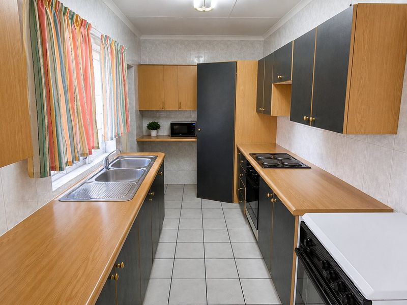 A functional galley-style kitchen featuring laminate countertops, built-in cabinetry, an electric hob, and a double bowl stainless steel sink with tiled finishes.
