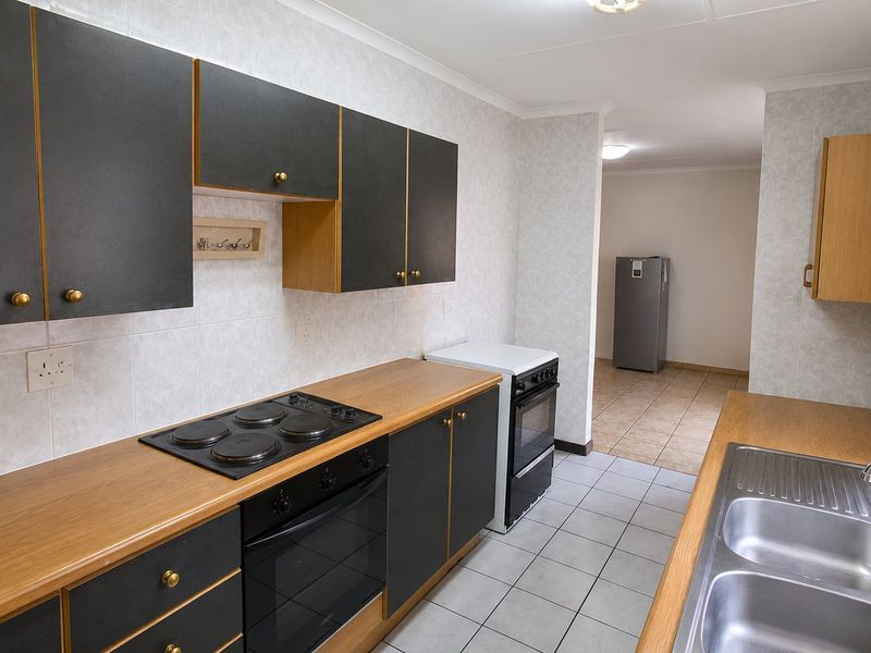 A functional kitchen featuring dark cabinetry, wood-look laminate countertops, an electric hob, built-in oven, and a double stainless steel sink with tiled flooring.