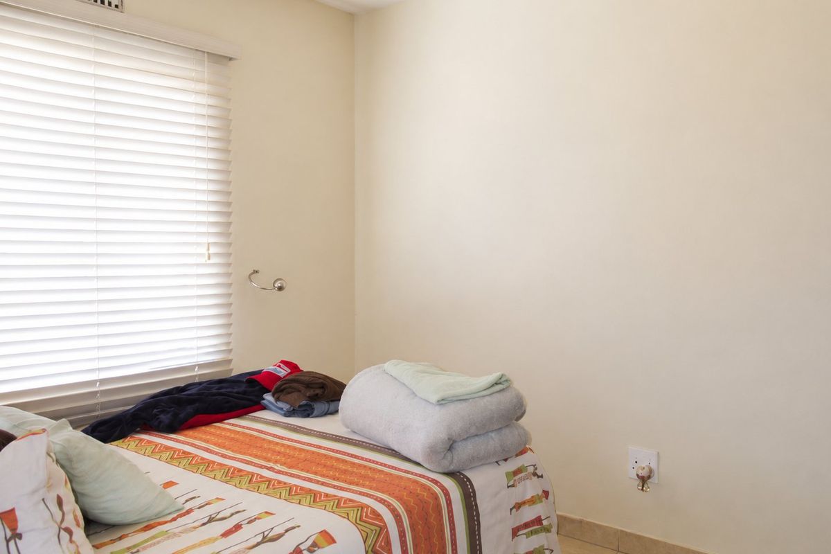 A bedroom featuring neutral walls, tiled flooring, and venetian blinds, providing a functional and well-lit space.