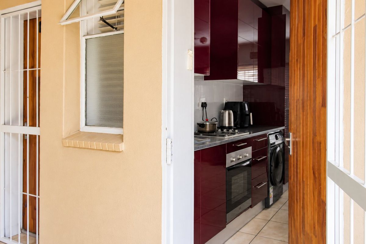 Compact kitchen featuring modern high-gloss cabinetry, built-in oven, hob, and integrated laundry appliance, accessible via a secure exterior door.