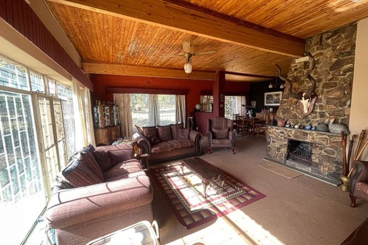 Spacious living room featuring a prominent stone fireplace, exposed timber beam ceiling, and large windows providing ample natural light.