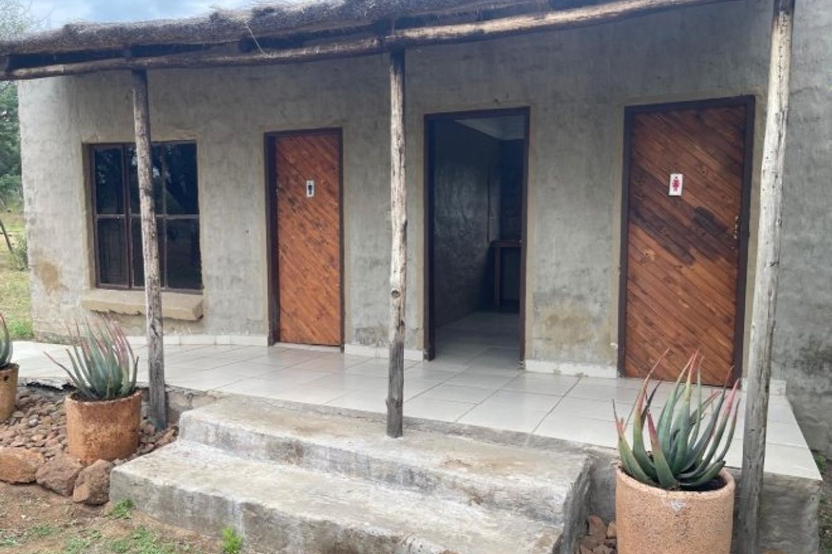 Rustic farm building exterior featuring a covered patio with a thatched roof, tiled flooring, and multiple wooden access doors.