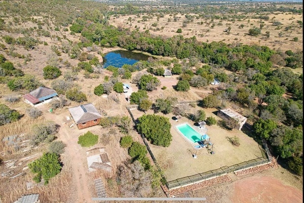 Aerial view of a rural farm property featuring multiple structures, a swimming pool, and a natural pond set within a large landscape.