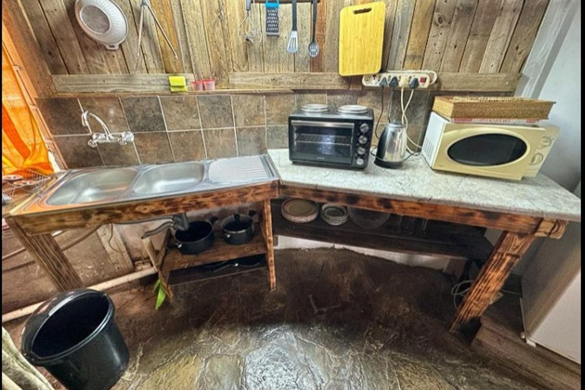 Rustic kitchen area featuring a double bowl stainless steel sink, stone countertop, and timber wall cladding with a natural stone floor finish.