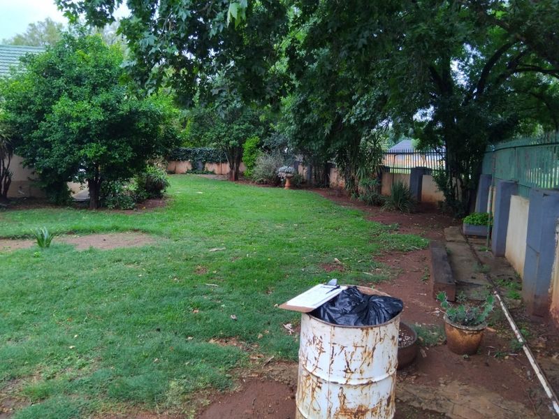 A spacious rear garden featuring mature trees, established lawn, and perimeter boundary walls with metal fencing.