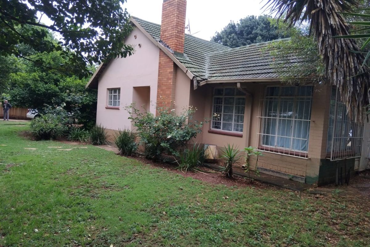 A view of the rear elevation of a single-story house featuring a brick chimney, tiled roof, and security-barred windows set within a garden.