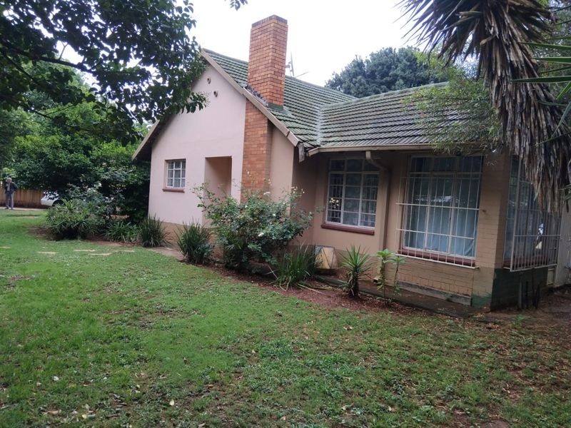 A view of the rear elevation of a single-story house featuring a brick chimney, tiled roof, and security-barred windows set within a garden.