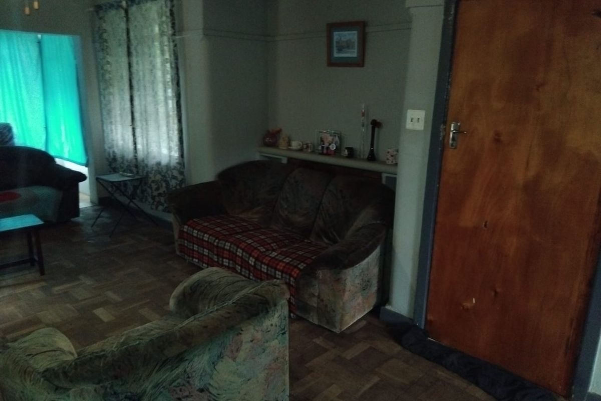 A living room featuring traditional parquet flooring, a timber door, and a picture rail, offering a dated interior space with potential for modernization.