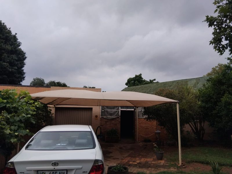 Front exterior view of the property featuring a brick facade, tiled roof, and a shade sail covering the paved driveway area.