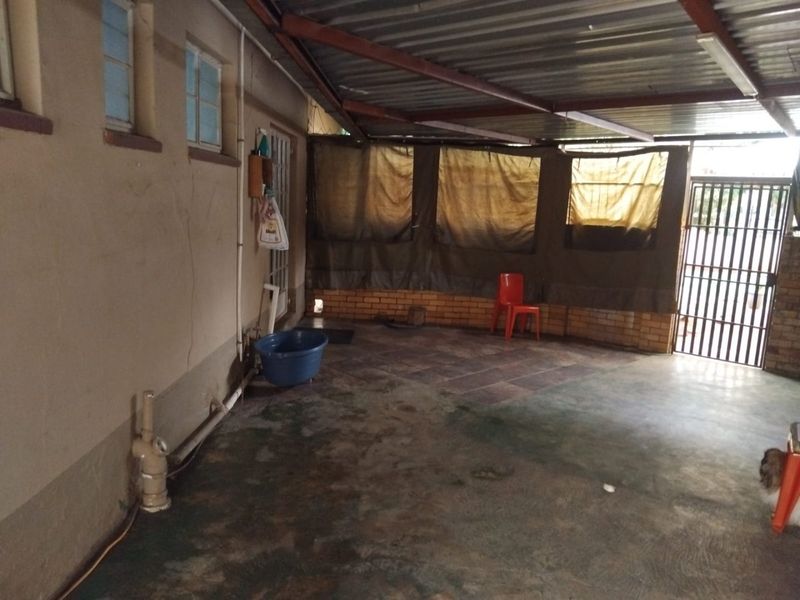 A covered outdoor patio area featuring a corrugated metal roof, brick wall accents, and tiled flooring, providing a functional space for outdoor living.
