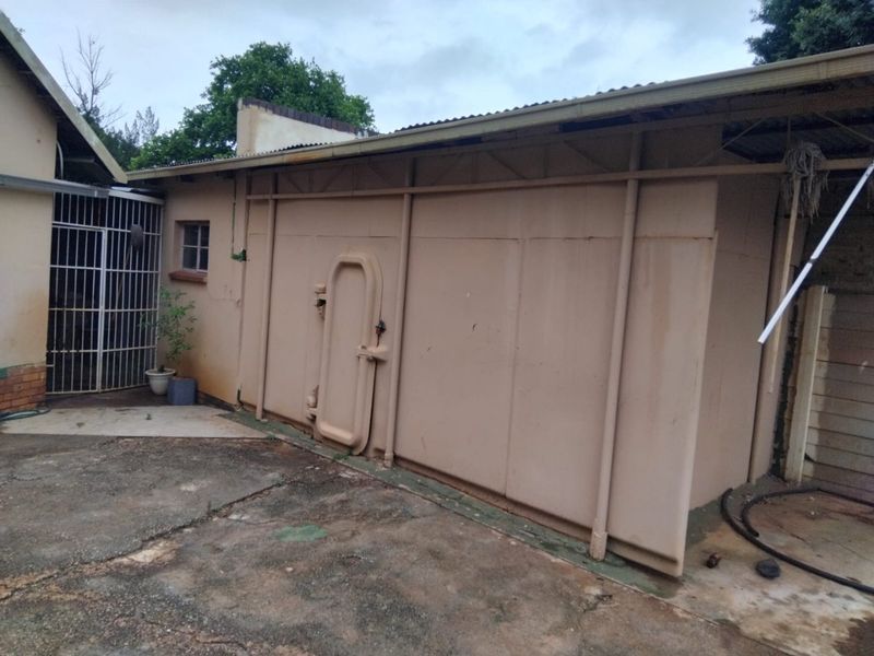 Rear exterior view of the property featuring a utility structure with industrial-style door, security gate, and concrete paved area.