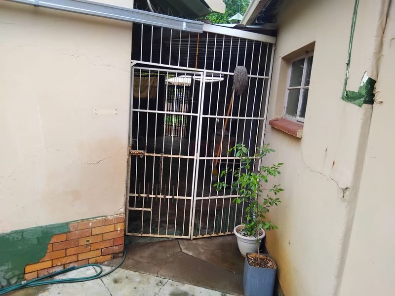 A rear exterior view showing a security gate entrance with visible wear to the exterior wall plaster and brickwork.