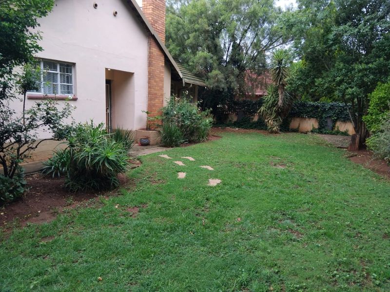 A rear garden view featuring a lawn area, established trees, and the side elevation of the house with a brick chimney.