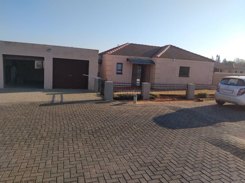 Front view of a single-story house featuring a tiled roof, paved driveway, and an attached garage with a secure metal fence.