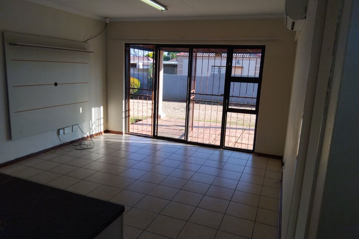 An empty living room featuring tiled flooring, wall-mounted air conditioning, and sliding glass doors providing access to the rear patio area.
