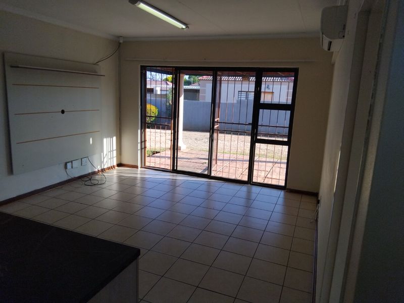 An empty living room featuring tiled flooring, wall-mounted air conditioning, and sliding glass doors providing access to the rear patio area.