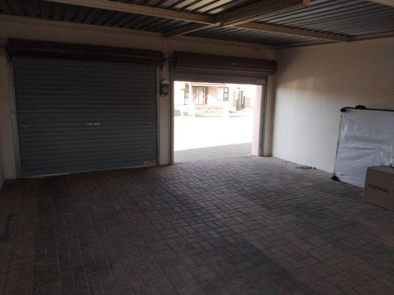 A spacious double garage featuring paved flooring, corrugated metal ceiling, and two roller shutter doors.