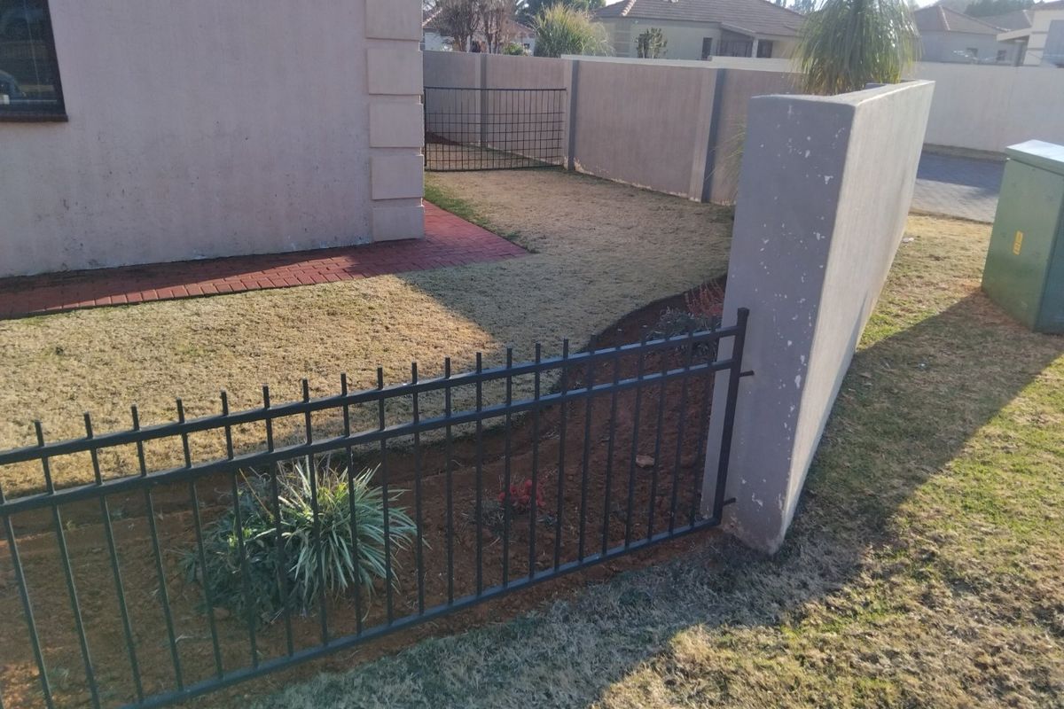 A view of the rear garden area featuring a paved walkway, perimeter boundary wall, and metal fencing.
