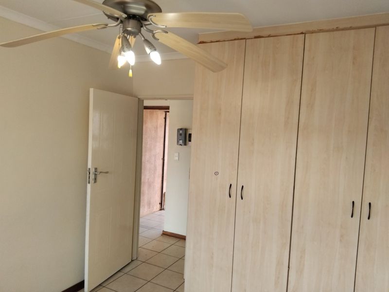 A vacant bedroom featuring built-in light wood cupboards, a ceiling fan, and tiled flooring, with visible wear on the cupboard trim.