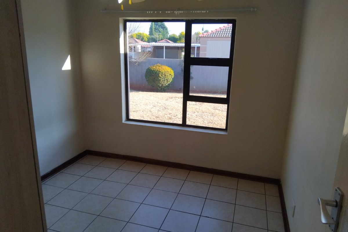 An empty bedroom featuring tiled flooring, a ceiling fan, and a large window providing natural light and a view of the rear garden.