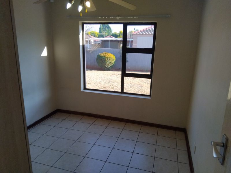 An empty bedroom featuring tiled flooring, a ceiling fan, and a large window providing natural light and a view of the rear garden.
