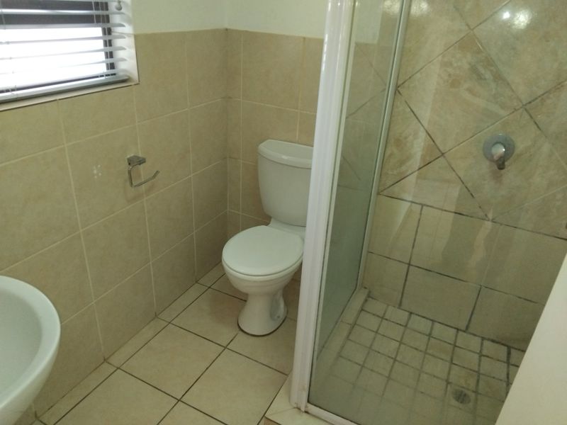 A functional bathroom featuring a shower enclosure, toilet, and neutral wall and floor tiling.