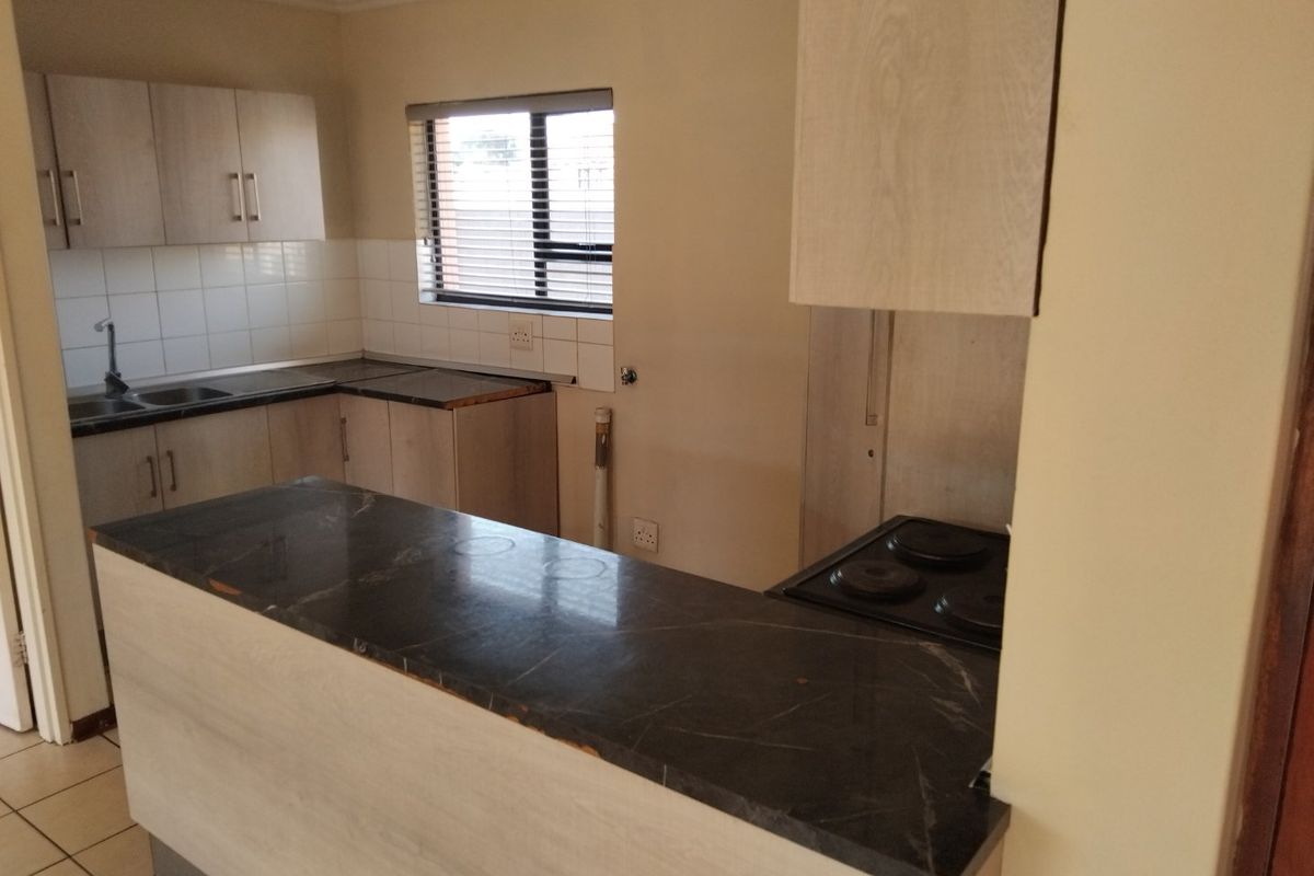 A functional kitchen featuring light wood-finish cabinetry, dark laminate countertops, a built-in electric hob, and tiled flooring, offering a clean, blank canvas for updates.