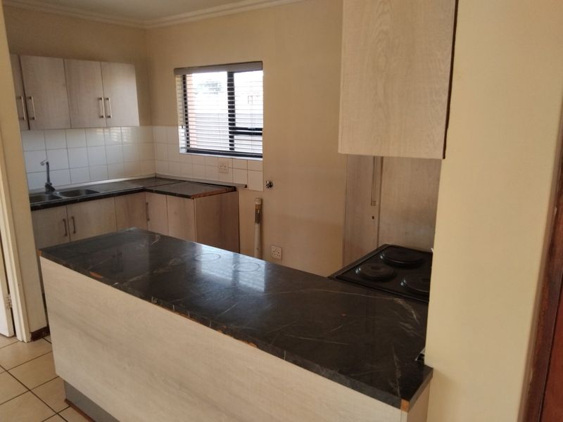 A functional kitchen featuring light wood-finish cabinetry, dark laminate countertops, a built-in electric hob, and tiled flooring, offering a clean, blank canvas for updates.