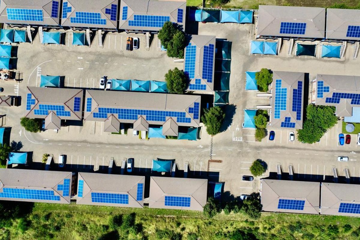 Aerial view of a commercial office park featuring multiple buildings with extensive rooftop solar panel installations and dedicated paved parking with shade cloth carports.