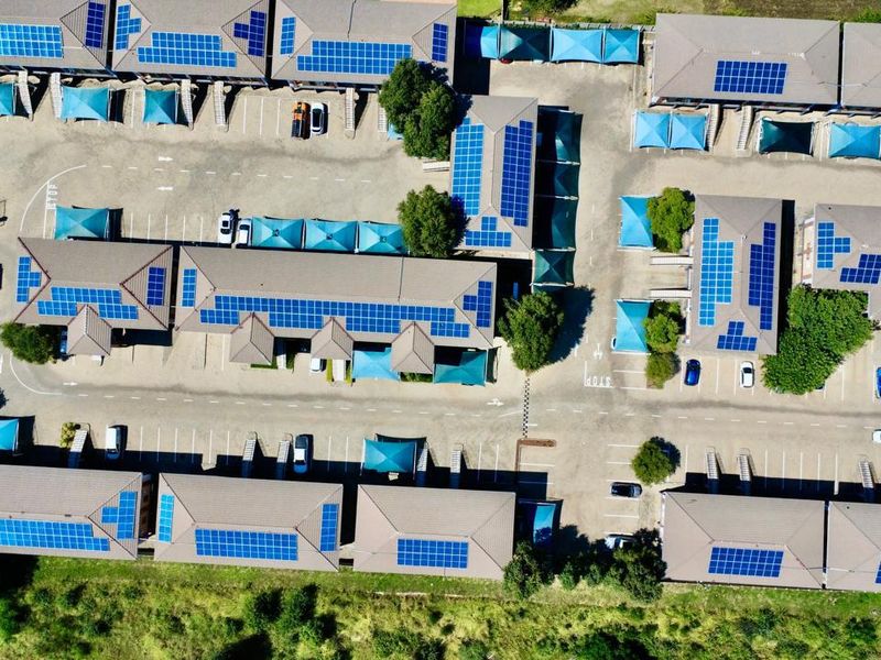 Aerial view of a commercial office park featuring multiple buildings with extensive rooftop solar panel installations and dedicated paved parking with shade cloth carports.