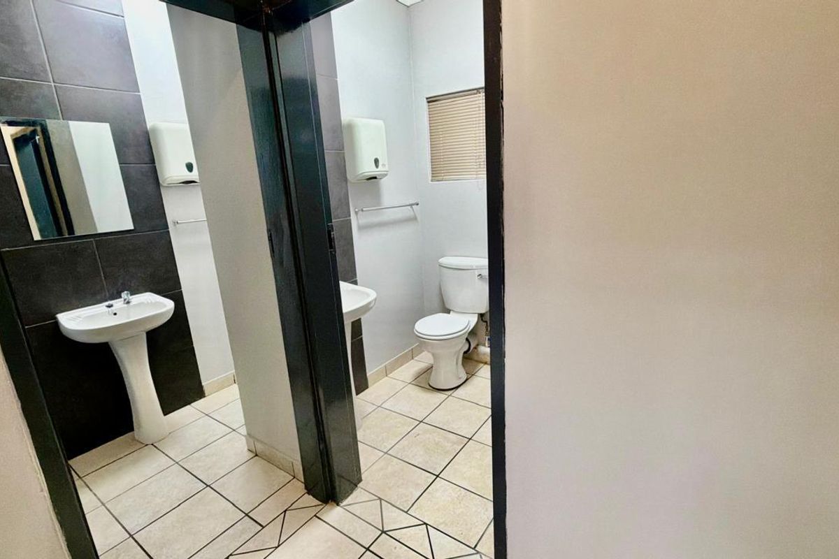 A functional commercial bathroom featuring a pedestal basin, tiled flooring, and a private toilet cubicle with neutral finishes.