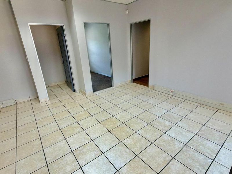 An empty commercial office space featuring neutral tiled flooring, electrical power skirting, and multiple access points to adjacent rooms.