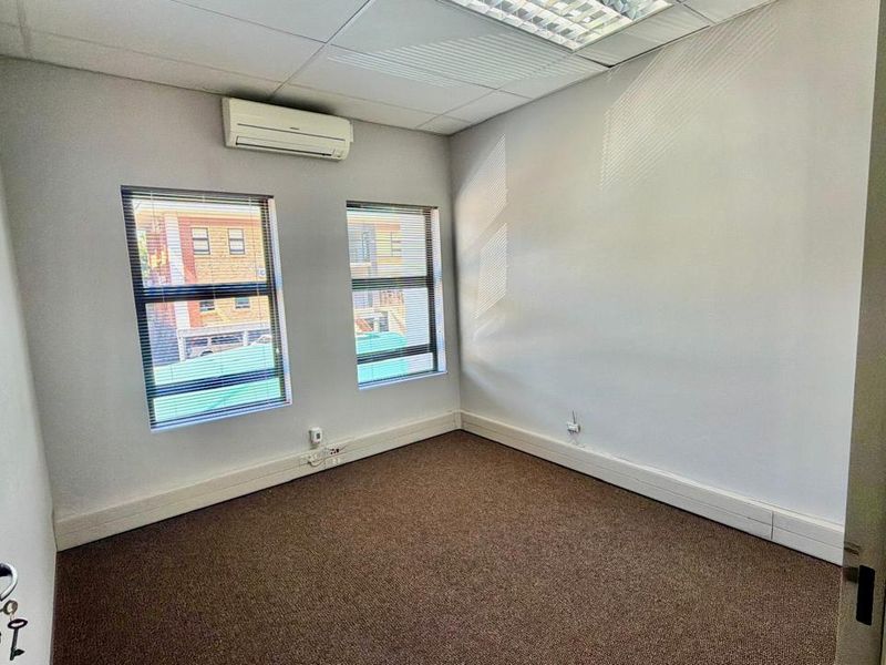 A clean, empty office space featuring carpet flooring, a suspended ceiling, and a wall-mounted split-system air conditioner.