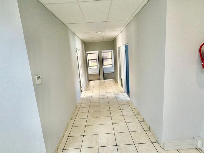 A clean, functional commercial hallway featuring tiled flooring, a suspended ceiling, and a wall-mounted fire extinguisher.