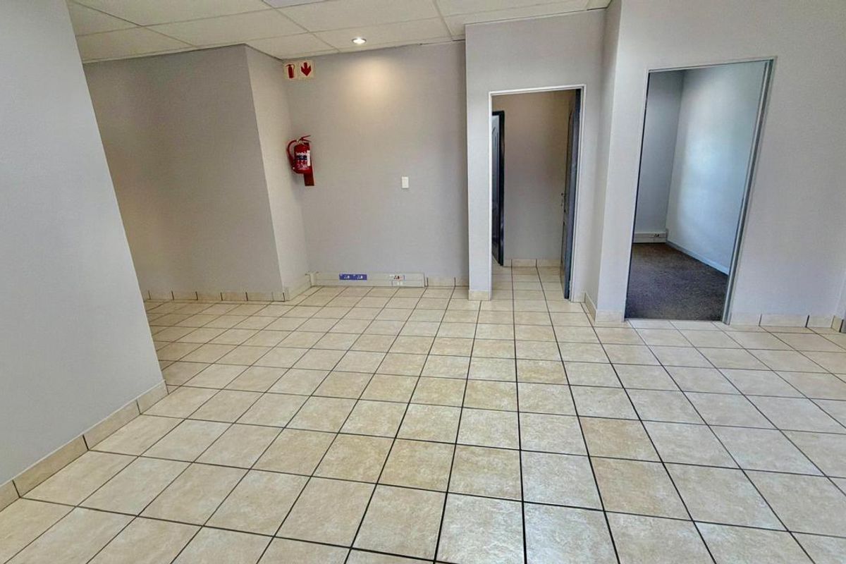 An empty commercial office space featuring neutral wall finishes, ceramic floor tiles, and a suspended ceiling with integrated lighting.