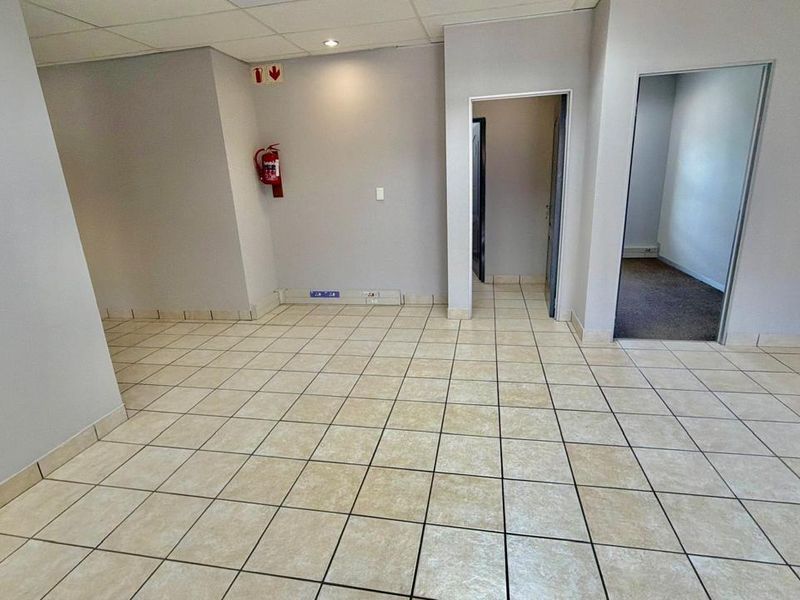 An empty commercial office space featuring neutral wall finishes, ceramic floor tiles, and a suspended ceiling with integrated lighting.