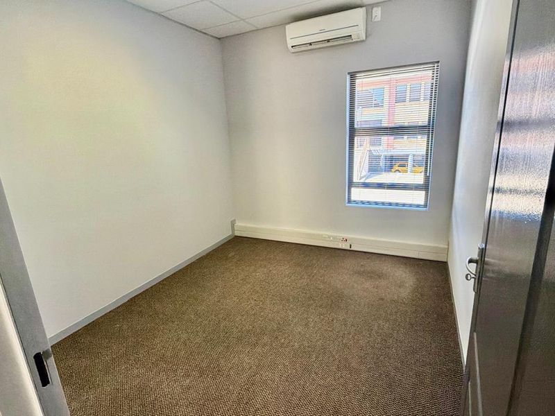 A clean, empty office space featuring carpeted flooring, a suspended ceiling, and a wall-mounted split-system air conditioning unit.