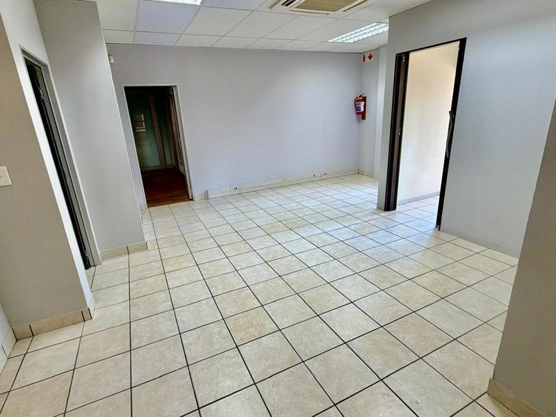 An empty commercial office space featuring ceramic tiled flooring, a suspended ceiling with recessed lighting, and an integrated air conditioning unit.