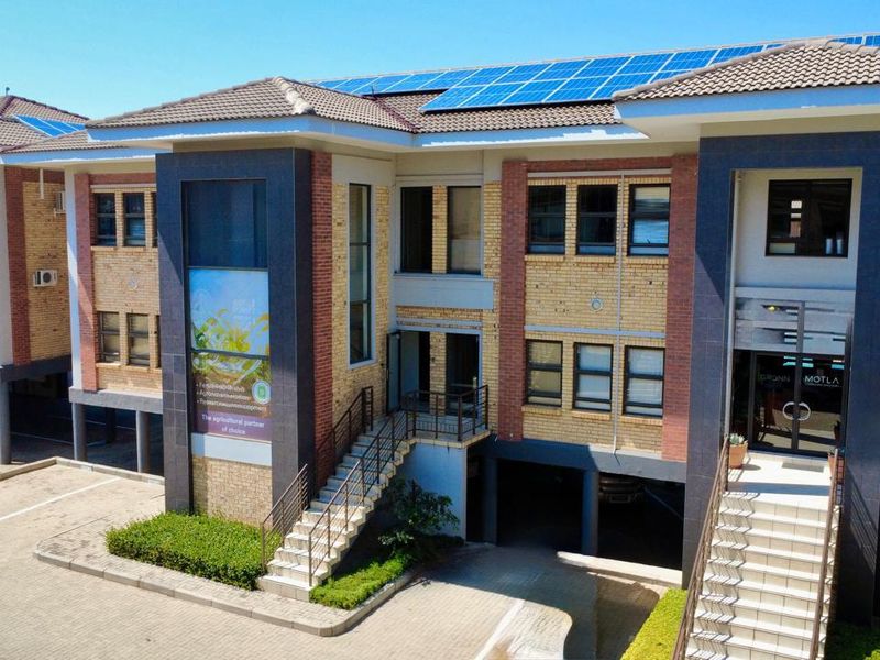 A modern commercial office building featuring a brick facade, tiled roof with integrated solar panels, external staircases, and covered parking facilities.