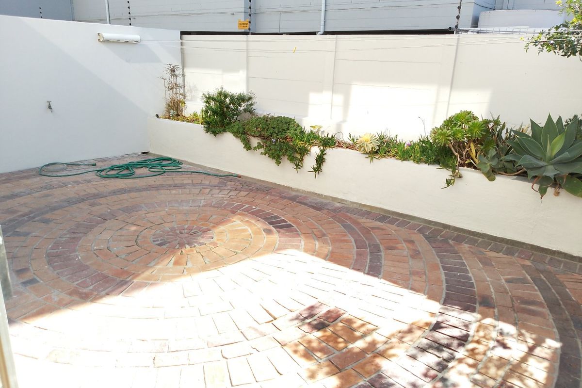 A private rear courtyard featuring decorative circular brick paving, a raised garden bed, and secure perimeter walling with electric fencing.