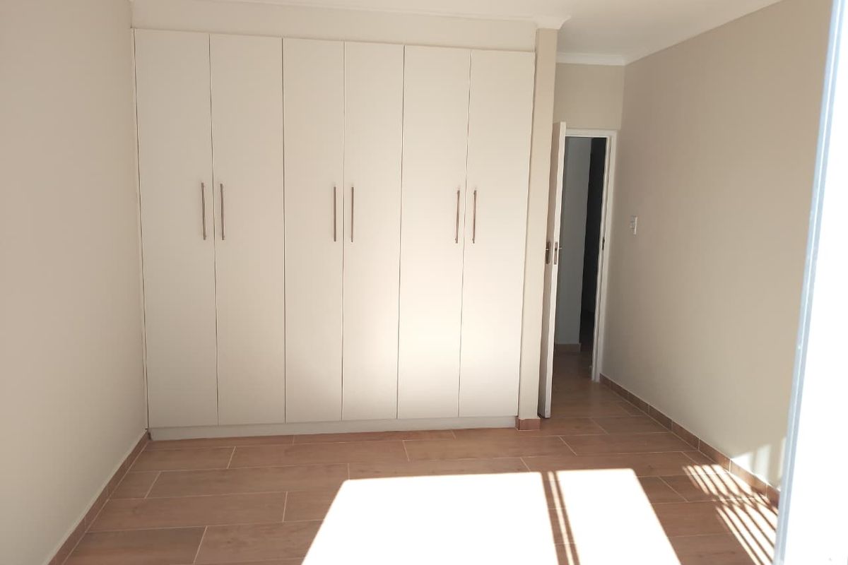 A bright, empty bedroom featuring neutral walls, modern wood-look tiled flooring, and extensive built-in cupboard storage.